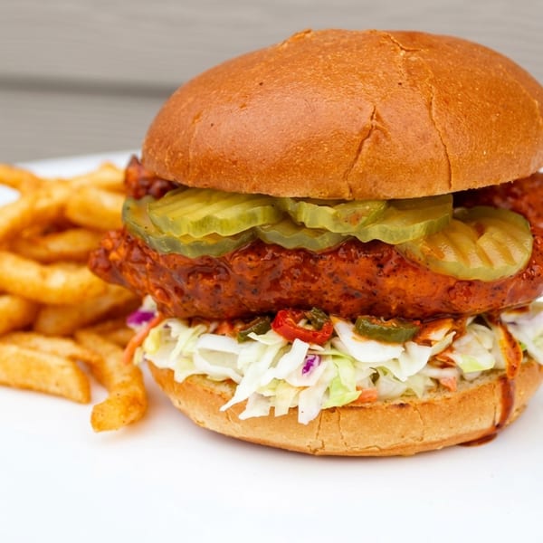 Spicy chicken sandwich with pickles, coleslaw, and jalapeños, served with a side of fries.