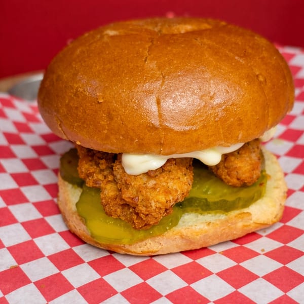 Crispy fried chicken sandwich with pickles and mayonnaise on a brioche bun, on red and white checkered paper.