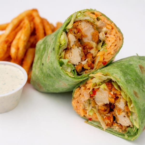 Chicken wrap cut in half, revealing chicken, lettuce, and cheese, with fries and dipping sauce.