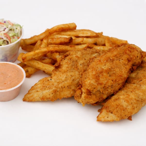 Crispy fried chicken tenders, golden french fries, coleslaw, and dipping sauce on a white background.